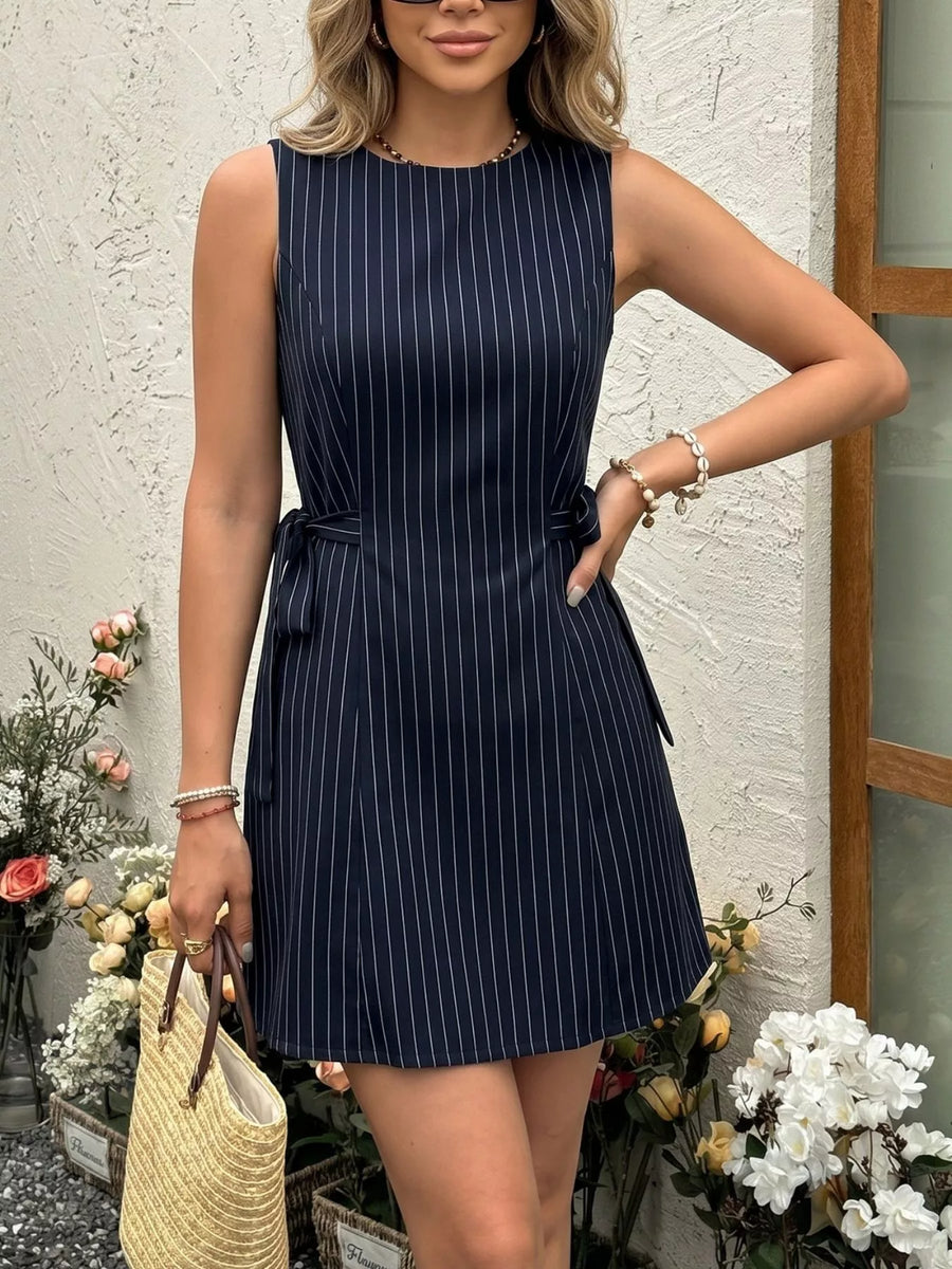 Front view of the Navy Blue Striped Sleeveless Tie Waist Dress, styled with feminine boutique styling for dinners, travel, and events, made for women who want elegant styling.